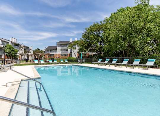 Community swimming pool with lounge chairs and trees in the background.