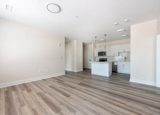 A spacious room with wooden flooring and a kitchen area in the background.
