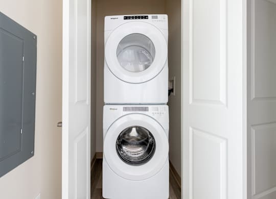 A white washing machine is stacked on top of another white washing machine in a narrow hallway.