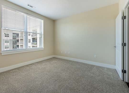 A room with a carpeted floor and a window with blinds.