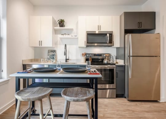 Model kitchen with stainless steel appliances and a counter with two stools