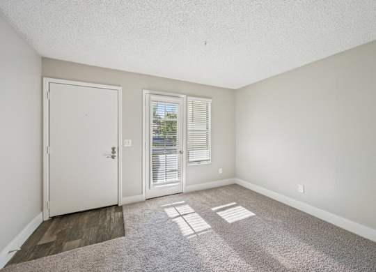 Model living room with a white door, a window with blinds, and a carpeted floor.