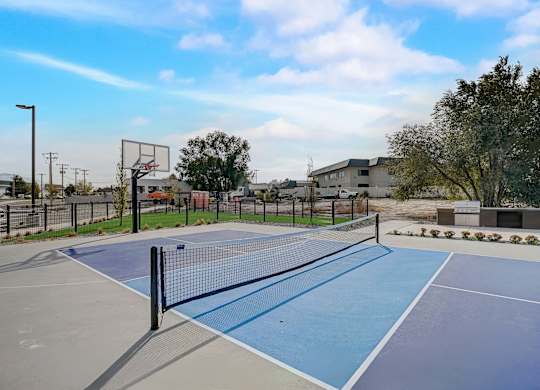 A tennis court with a net and a basketball hoop in the background.