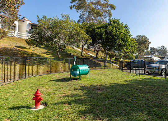 A green barrel sits on a grassy area next to a red fire hydrant.