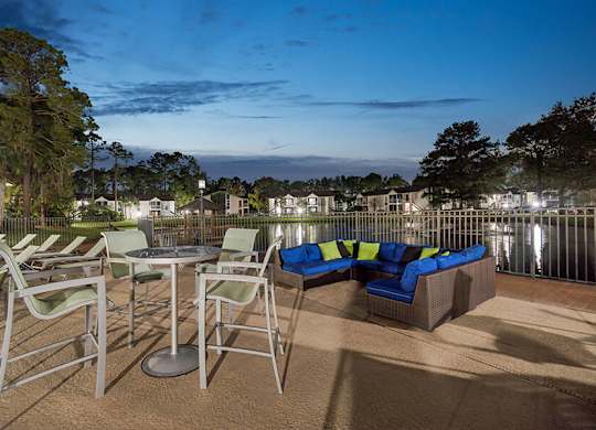 Outdoor BBQ Area with Lounge Furniture and View of Community Lake at Vue at Baymeadows Apartments located in Jacksonville, FL.