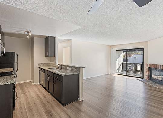 Model Kitchen with Dark Wood Cabinets, Wood-Style Flooring and Patio Accessibility at Santa Fe Ranch Apartments located in Carlsbad, CA.