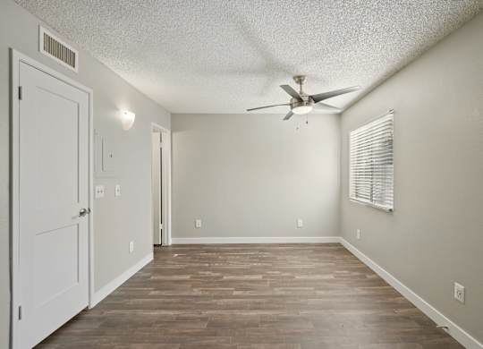 A room with a ceiling fan and wood-style flooring.
