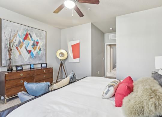 Model bedroom with a bed, a dresser, and a ceiling fan.