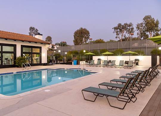 A pool with sun loungers and umbrellas in front of a building.