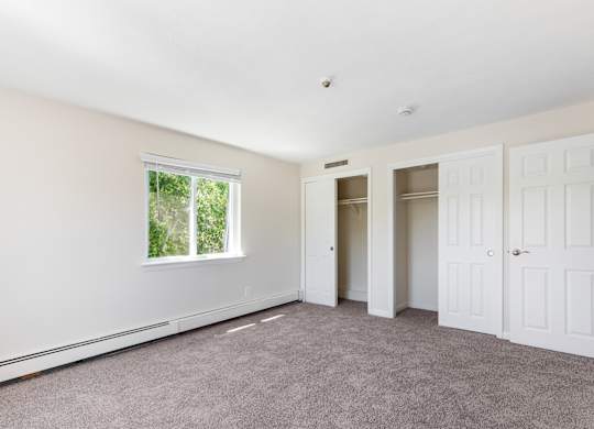 A room with white walls and a window with a view of trees.