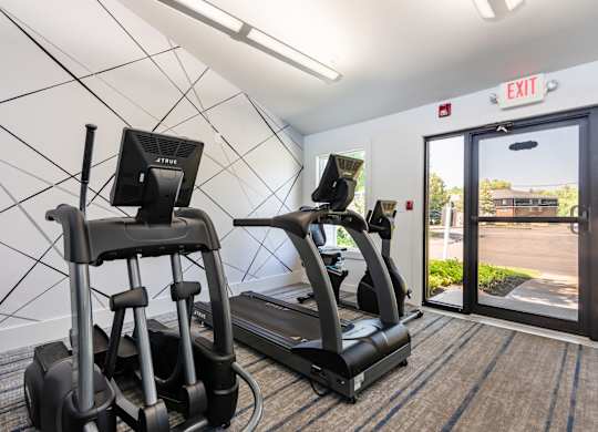 Two treadmills are in a room with a white wall and an exit sign.