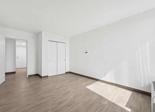 A room with white walls and wooden flooring with a rug in the middle.