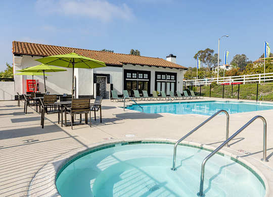 A pool with a ladder and a table with chairs and an umbrella outside a building.