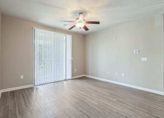 Model living room with a ceiling fan and sliding glass doors.