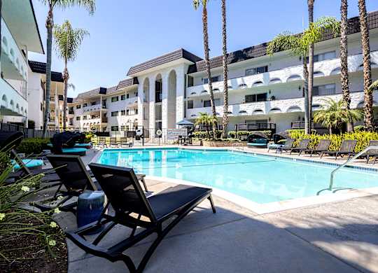 A pool surrounded by lounge chairs and palm trees.