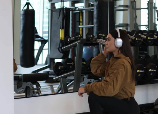 a woman sitting on a bench in a gym with headphones on