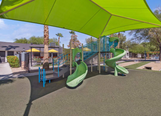 a playground with slides and a swing set under a green canopy
