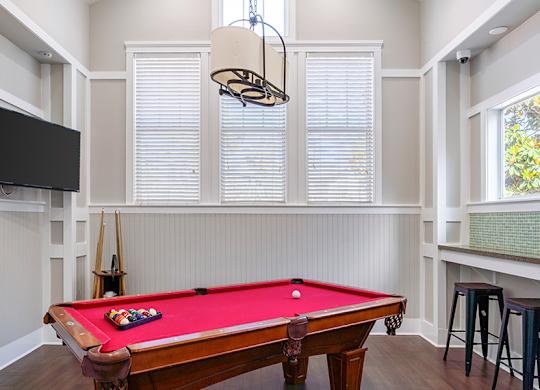 A pool table with a red cloth and a television on the wall.