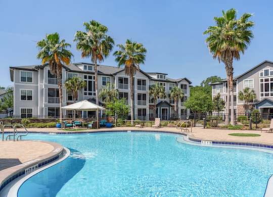 A swimming pool in front of a building with palm trees.