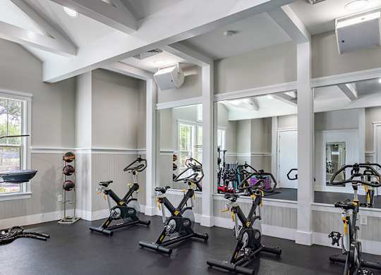 A gym with a row of stationary bikes and a mirror on the wall.