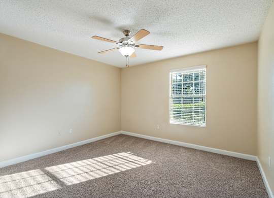 Model bedroom with carpet and a ceiling fan at Bridges at Bayside in St. Petersburg, Florida.