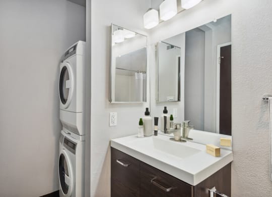 a bathroom with a sink and mirror next to a washer and dryer