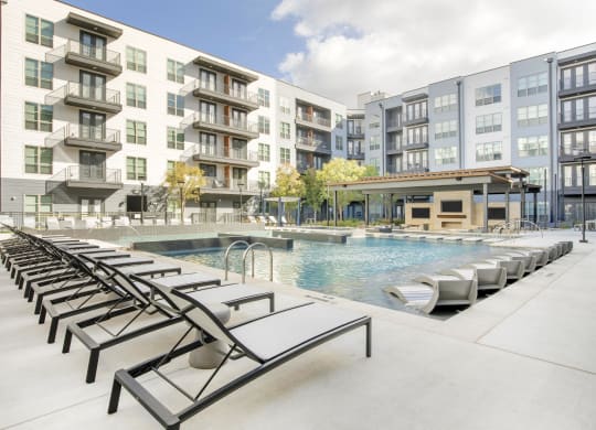 a swimming pool with lounge chairs in front of an apartment building