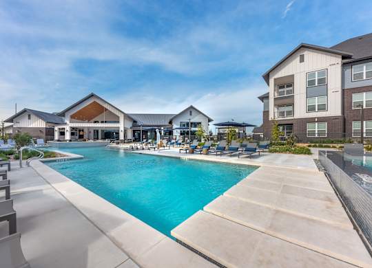 A large swimming pool is surrounded by a concrete patio and lounge chairs.