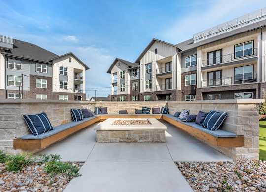 A modern outdoor seating area with benches and a fire pit in front of apartment buildings.