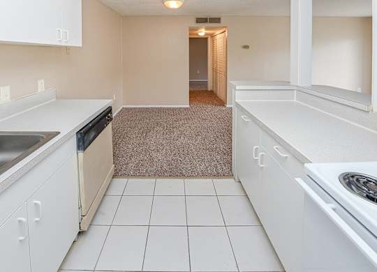 A kitchen with white cabinets and a beige carpet.