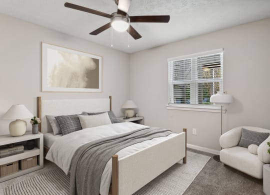 Sandy Springs, GA, Apartments Near MARTA - Edgewater at Sandy Springs - Bright Bedroom With Upholstered Bed, Ceiling Fan, Large Window With Blinds, And A Cozy Accent Chair.