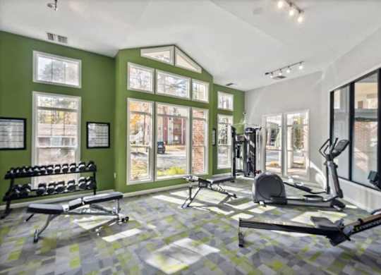 East Charlotte, NC, Apartments Near SouthPark Mall - Woodland Estates - A Fitness Center With Cardio Equipment, Free Weights, Workout Benches, Large Windows, And Green Accent Walls.