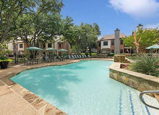Luxury Apartments for Rent in North Dallas, TX - Dallas North Park - A Swimming Pool With Clear Water, Lounge Chairs, Patio Umbrellas, Landscaped Deck, And Surrounding Apartment Homes.