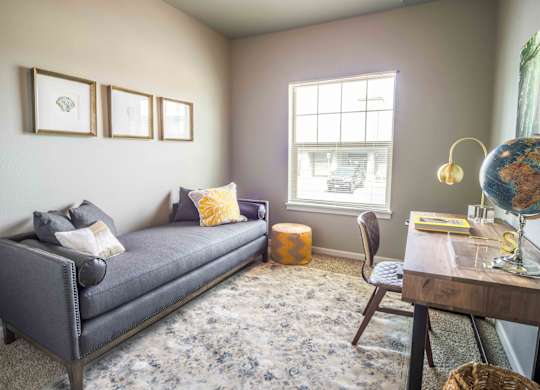A living room with a grey sofa, a wooden table, a chair, a globe, and a window.