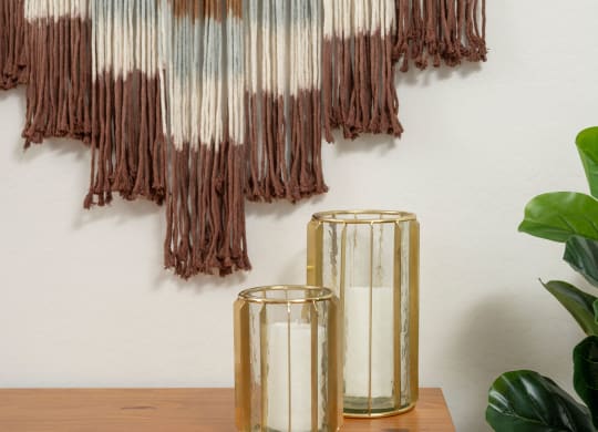 a piece of artwork hangs on a wall next to a table with two candles and a plant