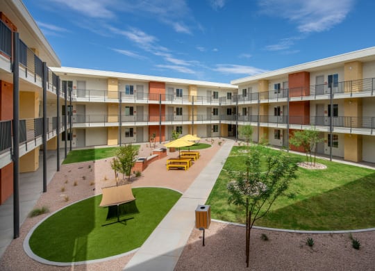 a courtyard with grass and tables and chairs in the middle of an apartment complex
