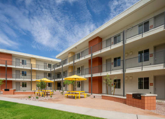 a courtyard with yellow tables and yellow umbrellas in front of an apartment building