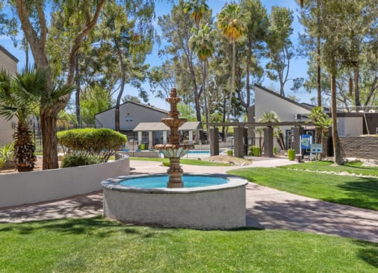 a fountain in the middle of a grassy area with apartments in the background