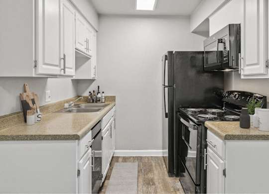 Pet-Friendly Affordable Apartments in East Tucson, AZ - Hampton Park - A Kitchen With White Cabinets, Tan Countertops, Double Sink, Black Refrigerator, Electric Stove, And Microwave.