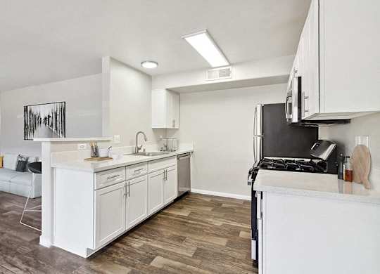 Model Kitchen with Wood-Style Flooring, White Cabinets and View of Living Room at Loma Vista Apartments in Las Vegas, NV.