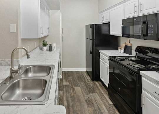 Dog-Friendly Apartments in Garland, TX - The Belmont at Duck Creek - A Kitchen With White Cabinets, Marble Look Countertops, Double Stainless Steel Sink, And Microwave.