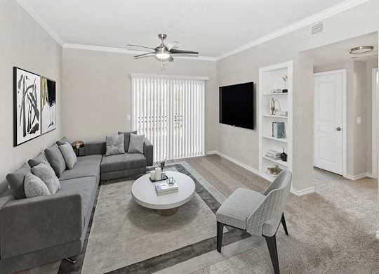Pet-Friendly Apartments in Garland, TX - The Belmont at Duck Creek - A Living Room With Gray Sectional Sofa, Round Coffee Table, Ceiling Fan Light, and Built-In Shelving.