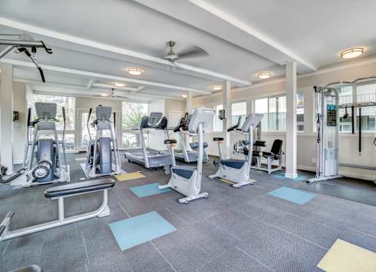 A spacious gym with a variety of equipment and a fan on the ceiling.