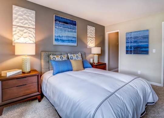 A bedroom with a large bed, two lamps, and two pictures on the wall.