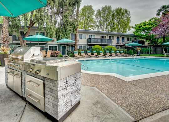 A poolside grill is in front of a pool and apartment building.