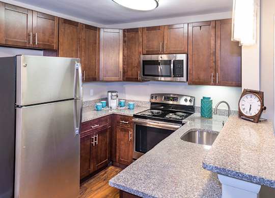 Model Kitchen with Dark Wood Cabinets and Wood-Style Flooring at Misty Ridge Apartments located in Woodbridge, VA.