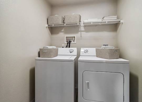 A small laundry room with two washing machines and a shelf above them.