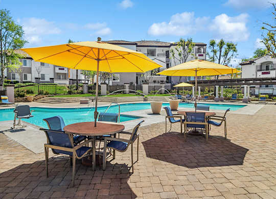 A poolside area with a table and chairs under a yellow umbrella.