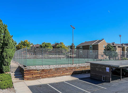 A tennis court surrounded by a fence and a parking lot.