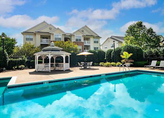 A swimming pool in front of a house with a gazebo.